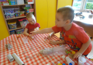 Dwóch chłopców przygotowuje stroje ekologiczne z papierowych rolek, worków plastikowych, sznurków.